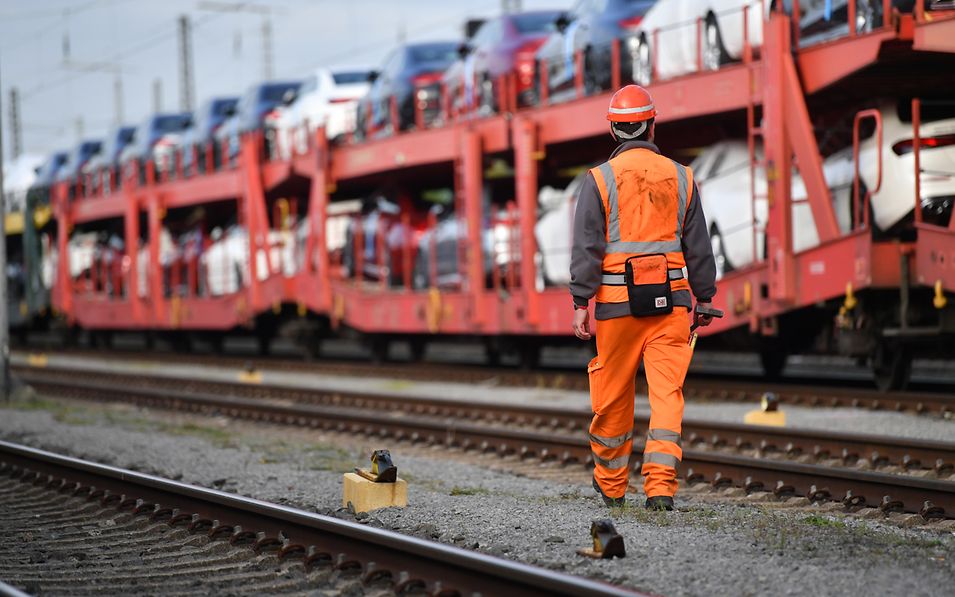 An operational staff member is walking alongside a freight train carrying finished vehicles.