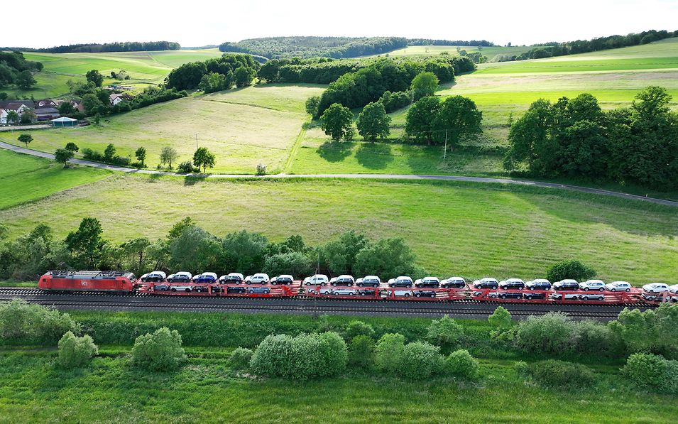 A freight train loaded with finished vehicles travels through green countryside